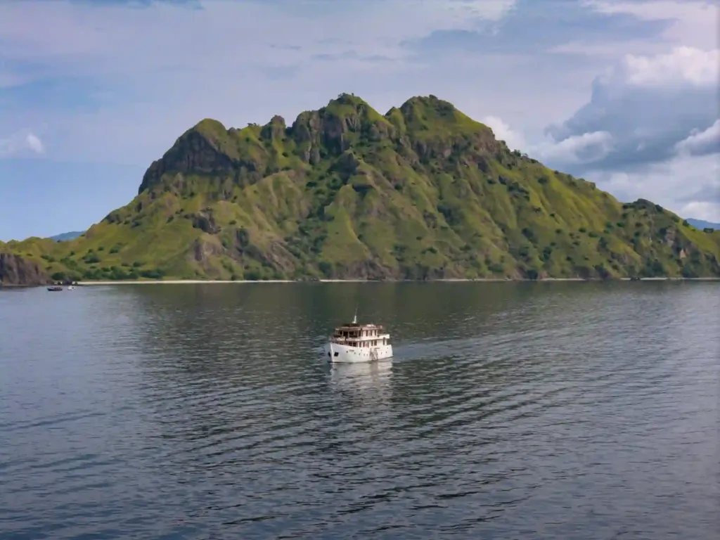 Komodo liveaboard vs day trip: a liveaboard at anchor below a green mountain in Komodo National Park